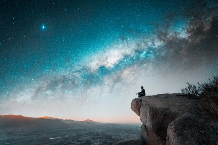 person sitting on the top of the mountain meditating or contemplating the starry night with Milky Way background